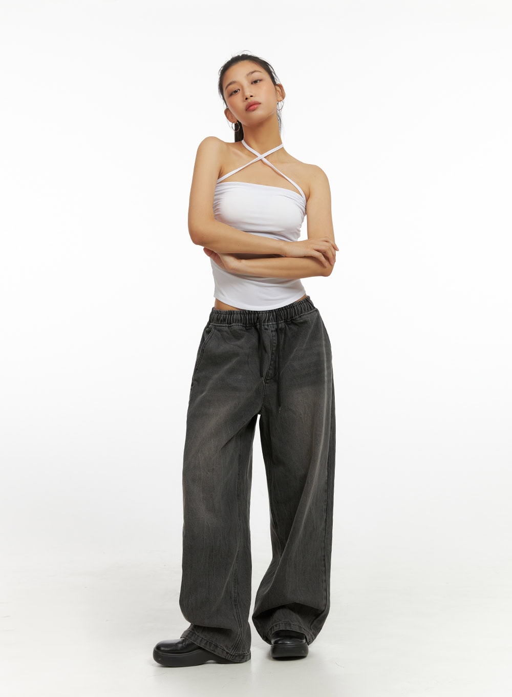 LEWKIN Banding Baggy Jeans IU412 in washed black, full-length front view on model, arms crossed, elastic waistband with drawstring, wide-leg cotton denim, paired with white halter crop top and black platform shoes.
