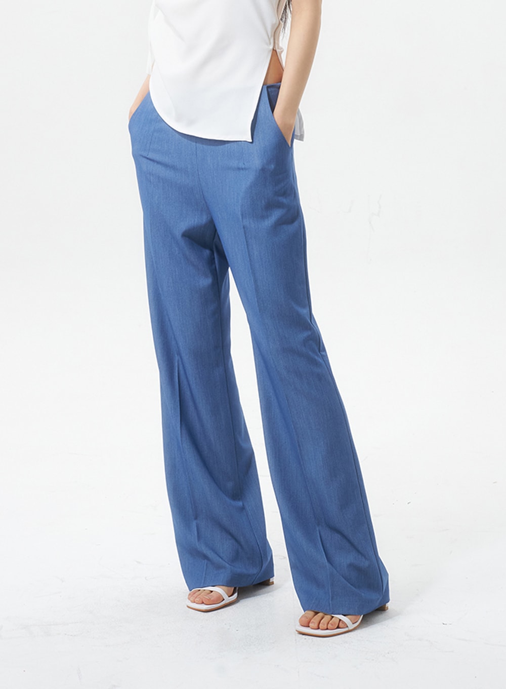LEWKIN Low Rise Tailored Pants IU326 in blue, side-angle close-up on model, wide-leg silhouette with front crease, hands in pockets, paired with white top and white sandals.