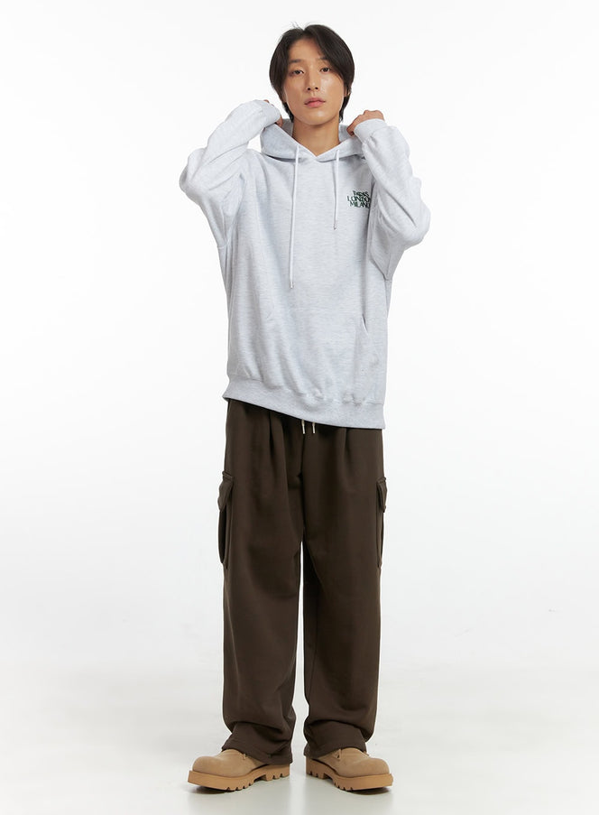 LEWKIN Men's Soft Cargo Pants IO417 in dark brown, full-length front view on model adjusting hood, wide-leg silhouette with side cargo pockets, paired with grey hoodie and tan boots.