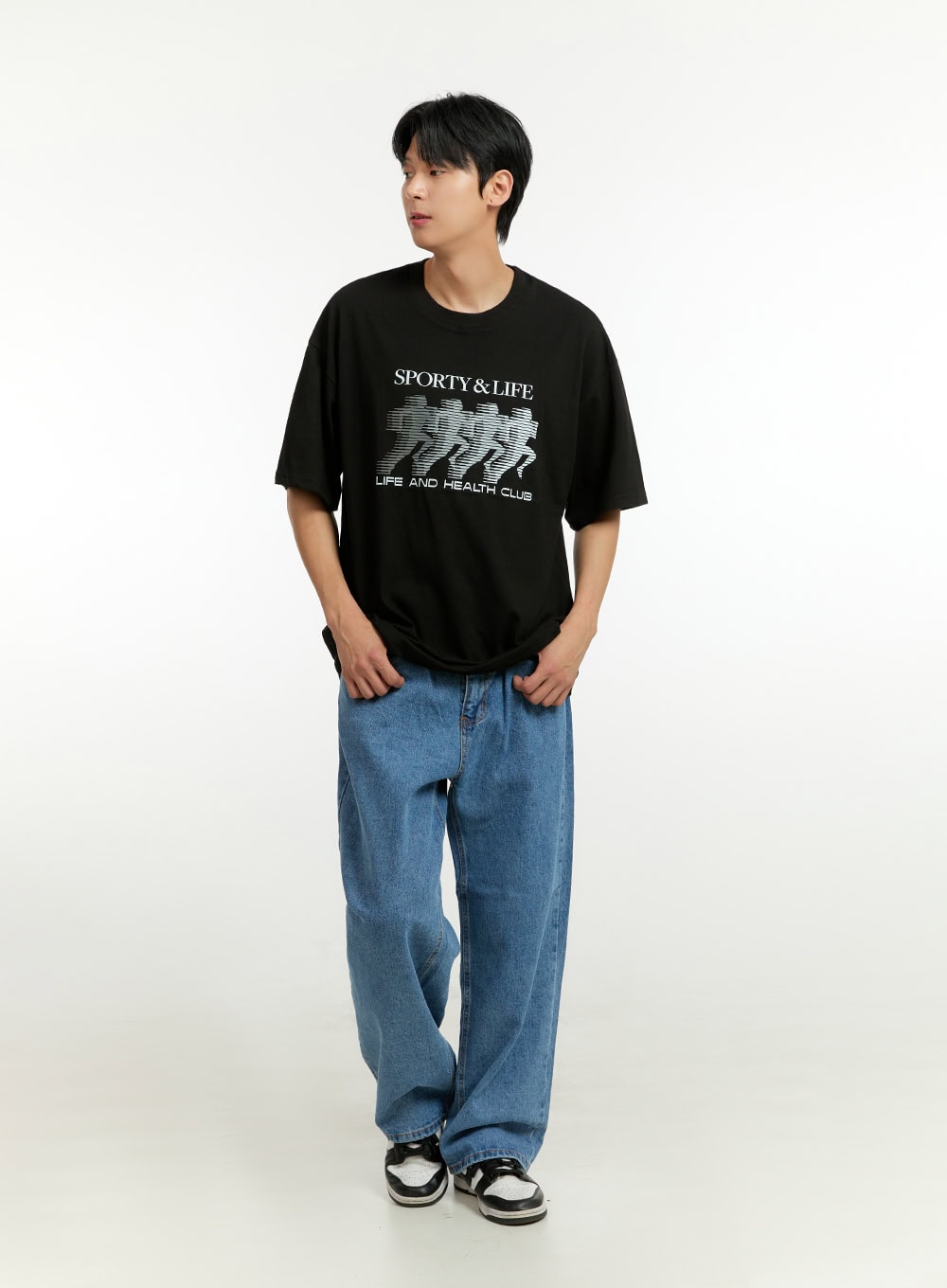 LEWKIN Men's Wide Fit Jeans IL412 in blue, full-length front shot on model looking sideways, relaxed wide leg denim, paired with black graphic tee and sneakers.