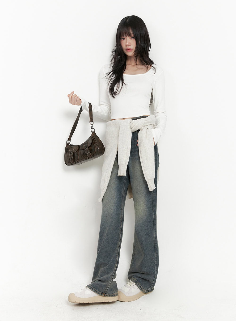 LEWKIN Asher Slimline Washed Bootcut Jeans ID402 in vintage blue, full-body editorial shot on model with cardigan tied at waist, white crop top, brown baguette bag, slim bootcut silhouette.