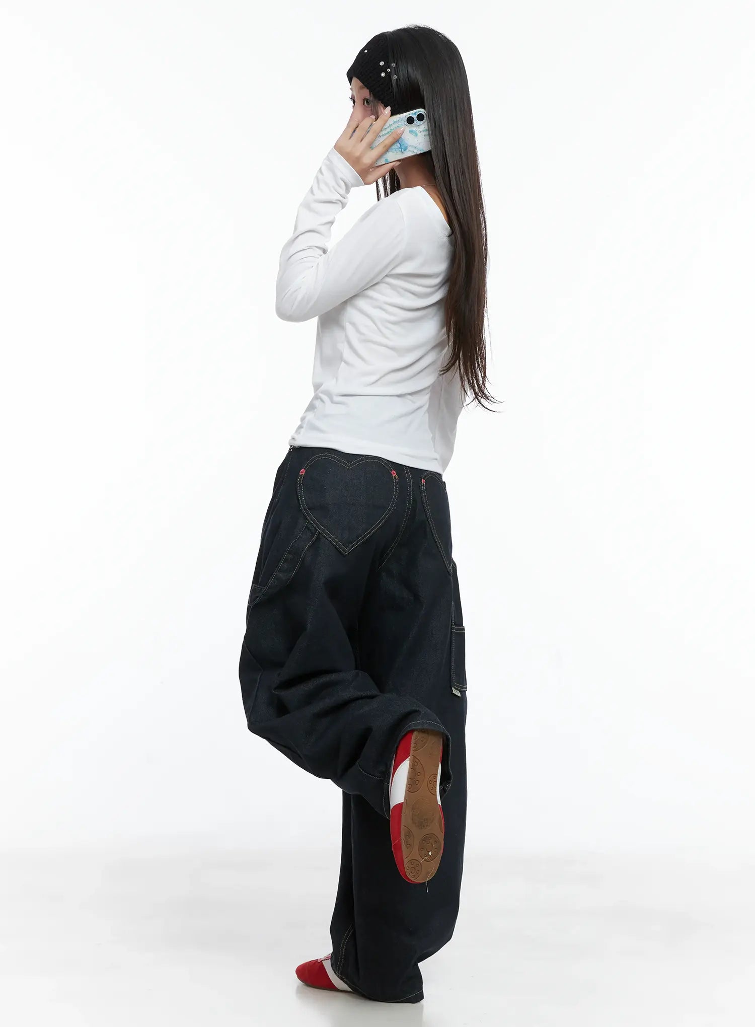 LEWKIN Heart Pocket Balloon Jeans CS503 in dark indigo, side view on model talking on phone, balloon silhouette with contrast stitching, paired with white long-sleeve top and red sneakers.