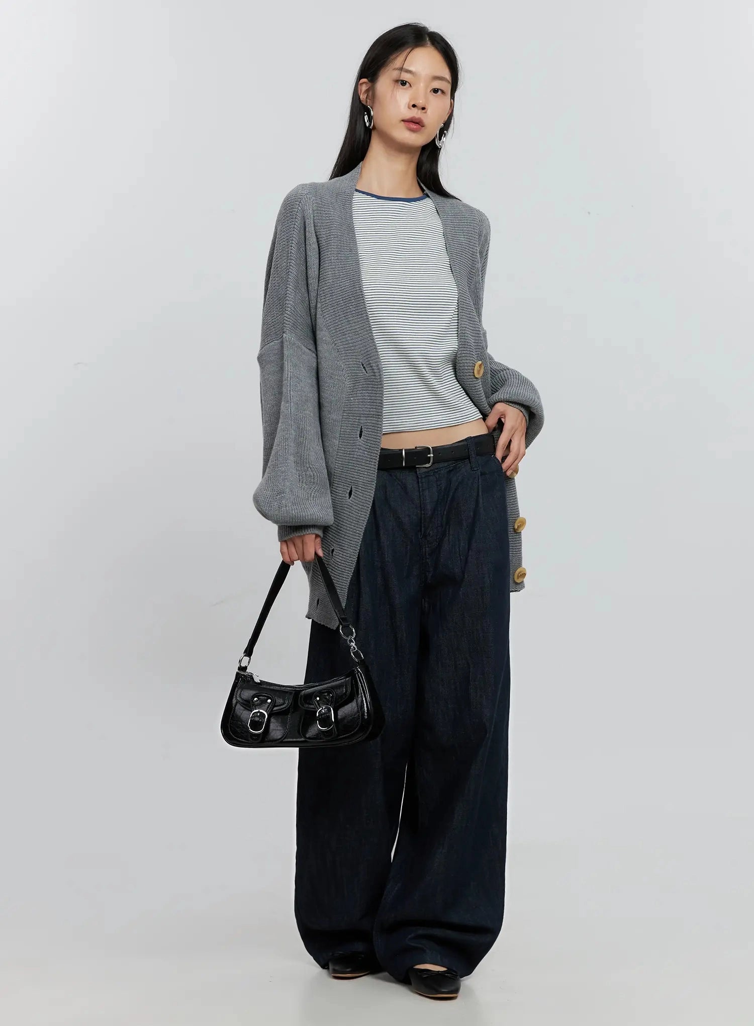 LEWKIN Elio Pintuck Wide-Leg Jeans IS516 in dark indigo, full-length front on model holding black shoulder bag, cotton wide-fit with pintuck pleats, styled with grey cardigan and black belt.