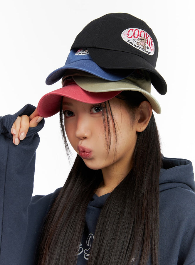 LEWKIN Bear Embroidered Graphic Cap IF421 in multi-color stack, model wearing four caps layered in black, navy, khaki, and pink, street-style close-up, cotton twill with oval COOKIE lettering patch.