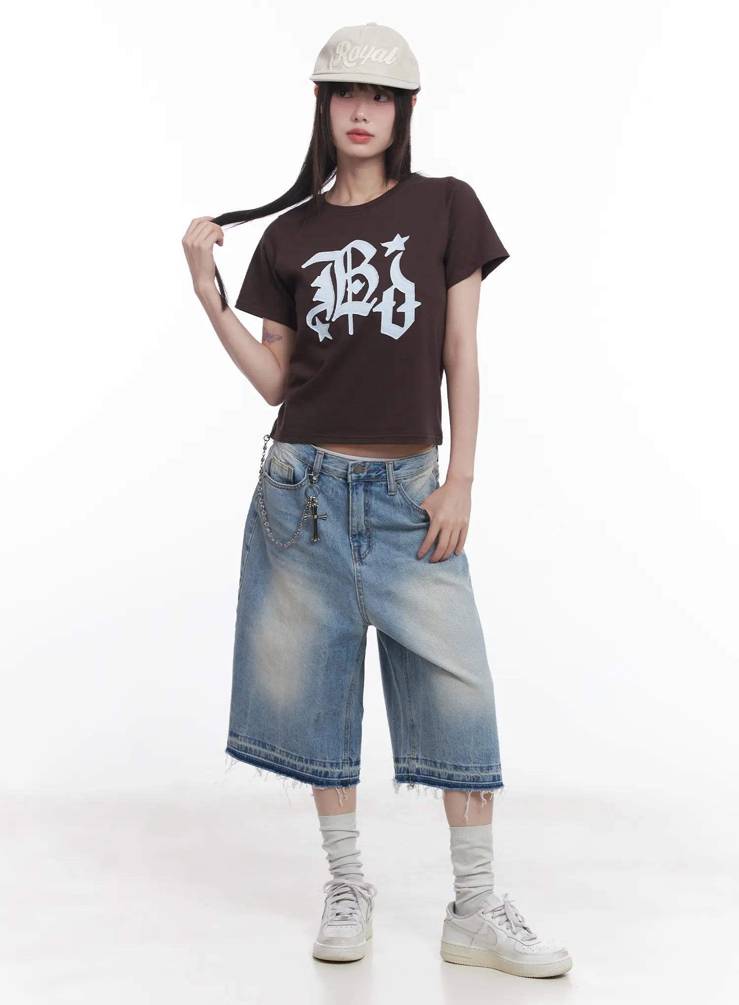 LEWKIN Light Wash Vintage Jorts CU519 in blue, full-body front on model with cap, wide-fit midi denim shorts, raw frayed hem, chain accessory, paired with brown graphic crop tee and white sneakers.