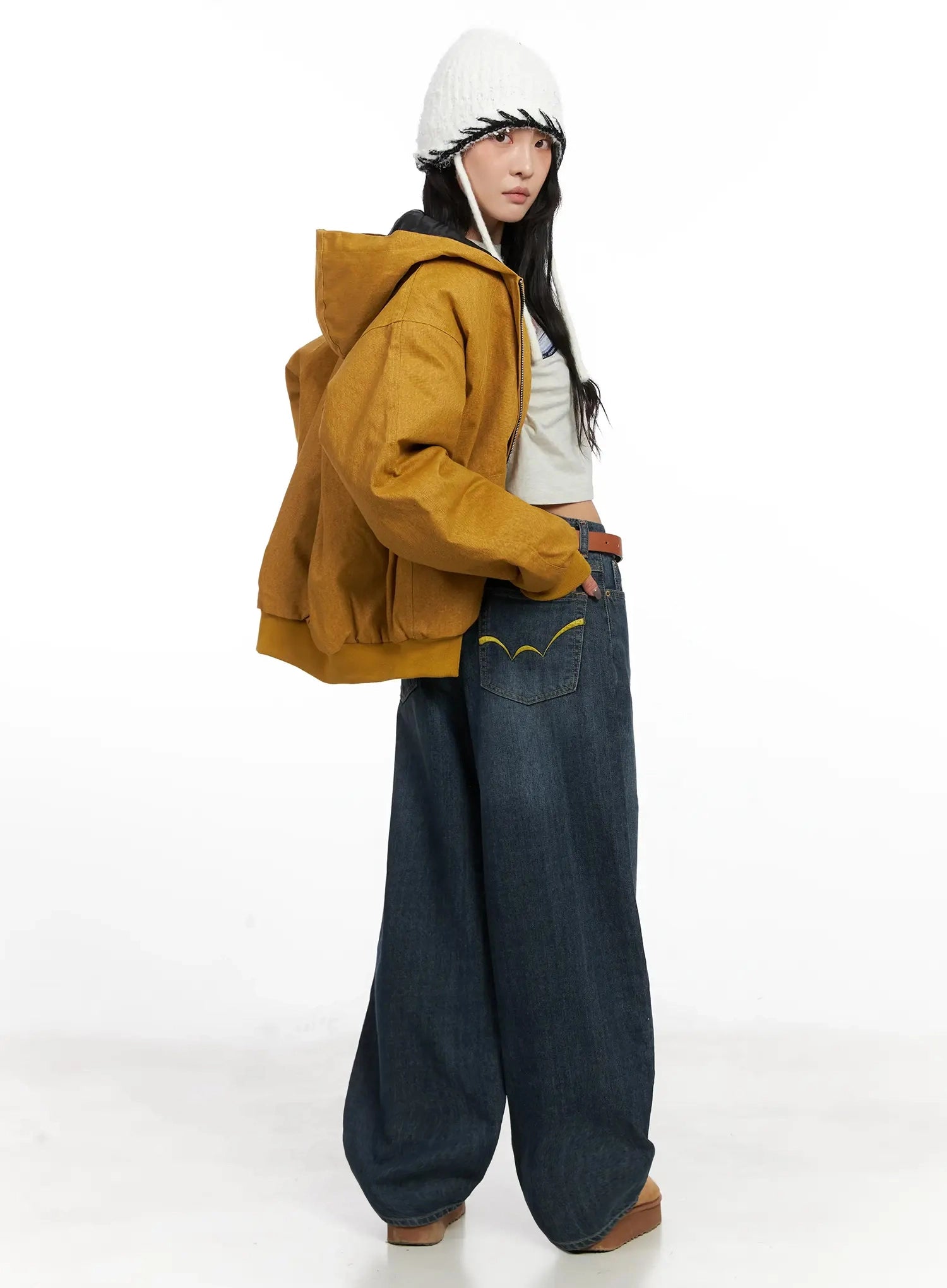 LEWKIN Regina Contrast Stitch Baggy Jeans IN528 in dark blue wash, side-back view on model, wide-leg cotton denim with yellow embroidery on back pocket, styled with mustard hoodie and white beanie.