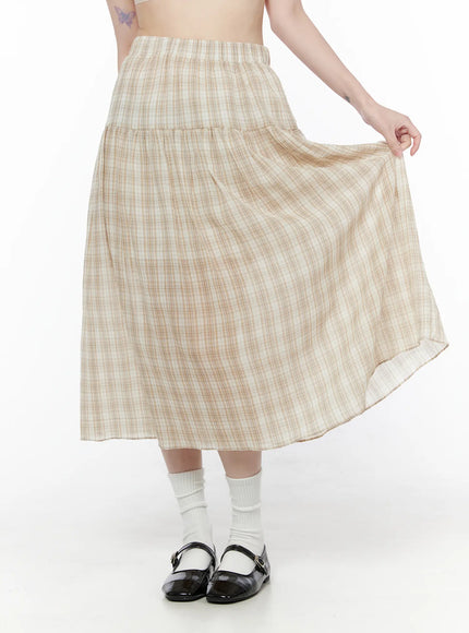 LEWKIN Plaid Flare Maxi Skirt CU519 in beige, front three-quarter view on model holding out skirt hem, tiered flare silhouette with elastic waist, lightweight plaid fabric, styled with white socks and black Mary Janes.