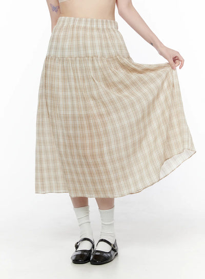 LEWKIN Plaid Flare Maxi Skirt CU519 in beige, front three-quarter view on model holding out skirt hem, tiered flare silhouette with elastic waist, lightweight plaid fabric, styled with white socks and black Mary Janes.