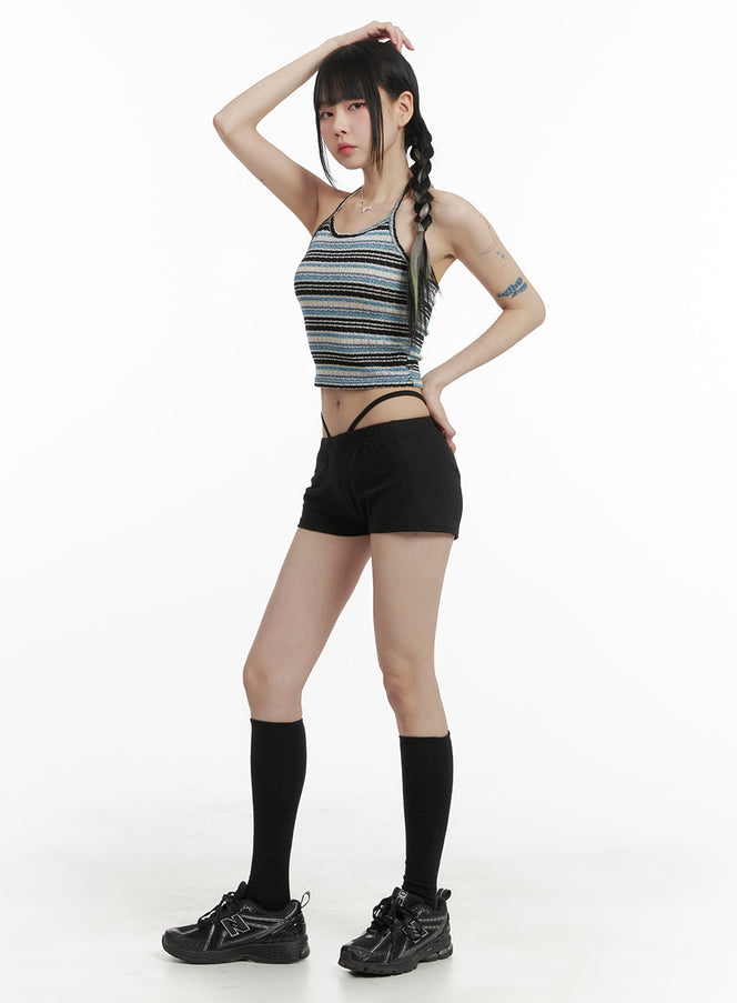 LEWKIN Waist Band Solid Inner Shorts OM426 in black, full-body side angle on model, slim-fit micro shorts with crossover waist strap, paired with striped crop top, knee socks, and chunky sneakers.