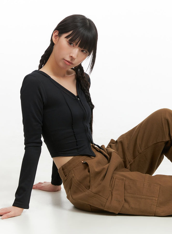 LEWKIN Hoodie Crop Top CG420 in Black, three-quarter front view on seated model, slim-fit zip-up with hood, long sleeves, paired with brown cargo pants.
