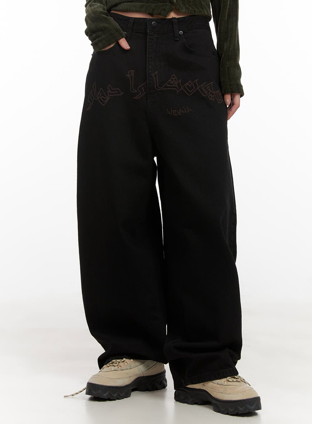 LEWKIN Yasmin Denim Wide Fit Jeans CD413 in black, front crop view on model, baggy cotton denim with dark tone-on-tone lettering print, paired with green ribbed top and chunky sneakers.