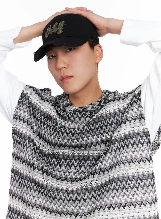 LEWKIN Men's NY Distressed Cap IG529 in black, worn by model with hands raised on crown, olive distressed NY embroidery, paired with zigzag knit hoodie, close-up portrait.
