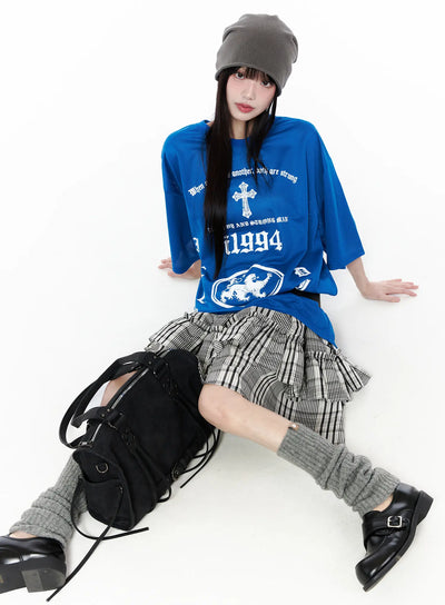 LEWKIN Plaid Layered Midi Skirt CU519 in black, full outfit on model seated on floor, two-tier ruffled skirt with elastic waist, styled with blue graphic tee, grey leg warmers, and black bag.