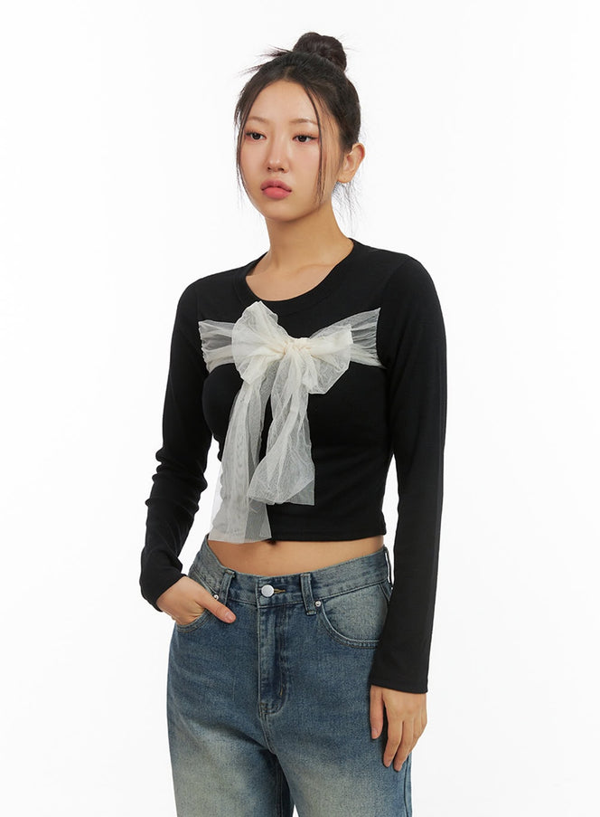 LEWKIN Ribbon Tied Long Sleeve Top IS402 in black, front bust-up shot on model, slim crop fit with sheer tulle bow detail at chest, paired with blue jeans.