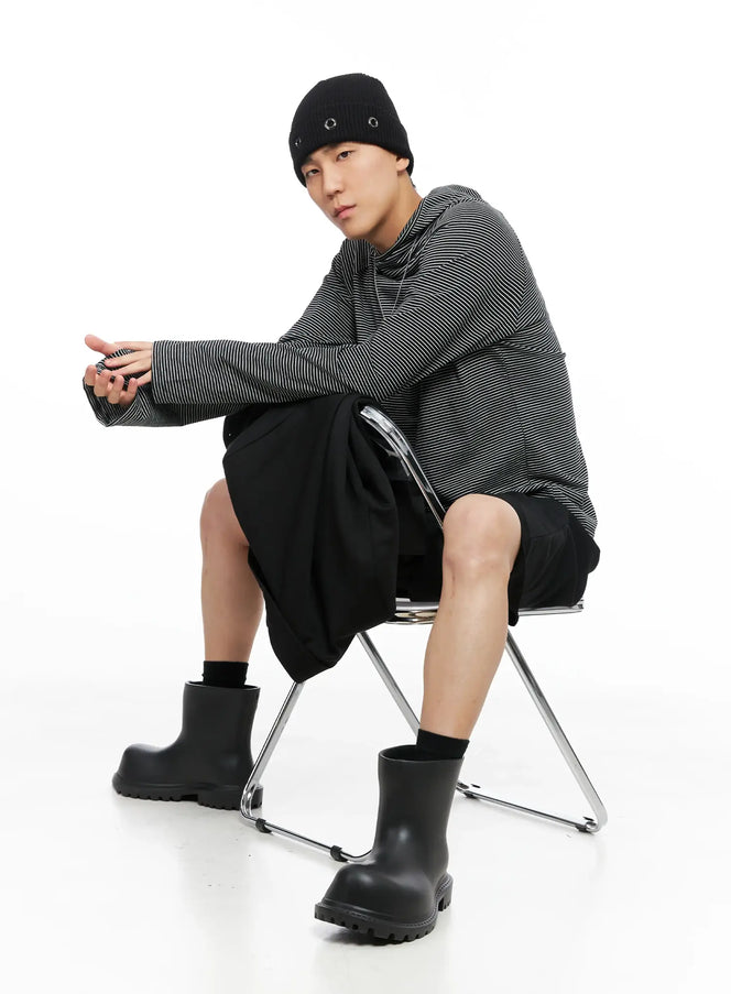 LEWKIN Men's Striped Long Sleeve Hoodie IS502 in black, editorial seated shot on model, fine horizontal stripe knit, paired with black shorts and rubber boots.