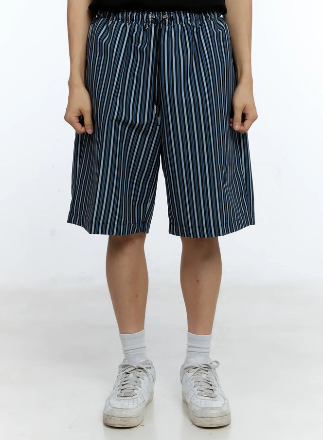 LEWKIN Men's Striped Straight-Leg Shorts IG515 in black, front close-up on model, wide-leg silhouette with elastic drawstring waist, blue and white vertical stripes, paired with white sneakers.