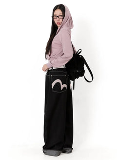 LEWKIN Kacey Plaid Stitched Back Pocket Baggy Jeans IM513 in black, side view on model with glasses, ultra-wide cotton denim with roll-up hem, plaid appliqué back pocket, paired with pink hoodie and black backpack.
