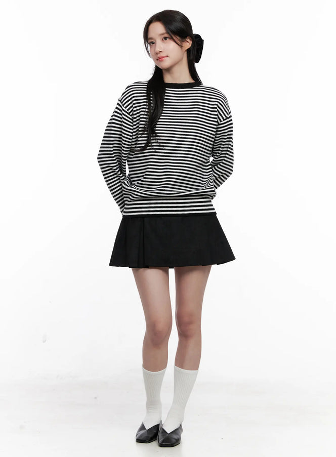 LEWKIN Chic Pleated Mini Skirt CO524 in black, full-body front on model, flare pleated polyester mini, banded waist, styled with black-white stripe knit sweater, white socks, black flats.