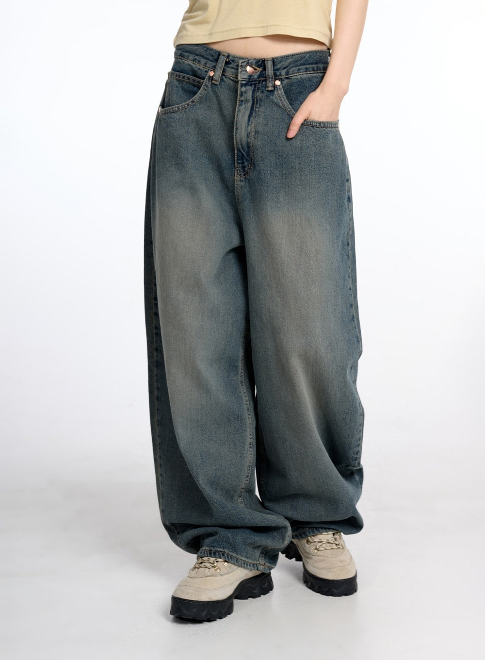 LEWKIN Vintage Low Rise Baggy Jeans CM415 in dark blue, front three-quarter view on model, wide-fit washed cotton denim with low rise waist and oversized pooling leg, paired with beige crop top and chunky sneakers.