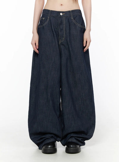 Rowen Baggy Jeans CU519 in dark blue, front view on model, ultra-wide balloon leg silhouette with contrast stitching and button waist, pooling at hem, paired with black leather shoes.