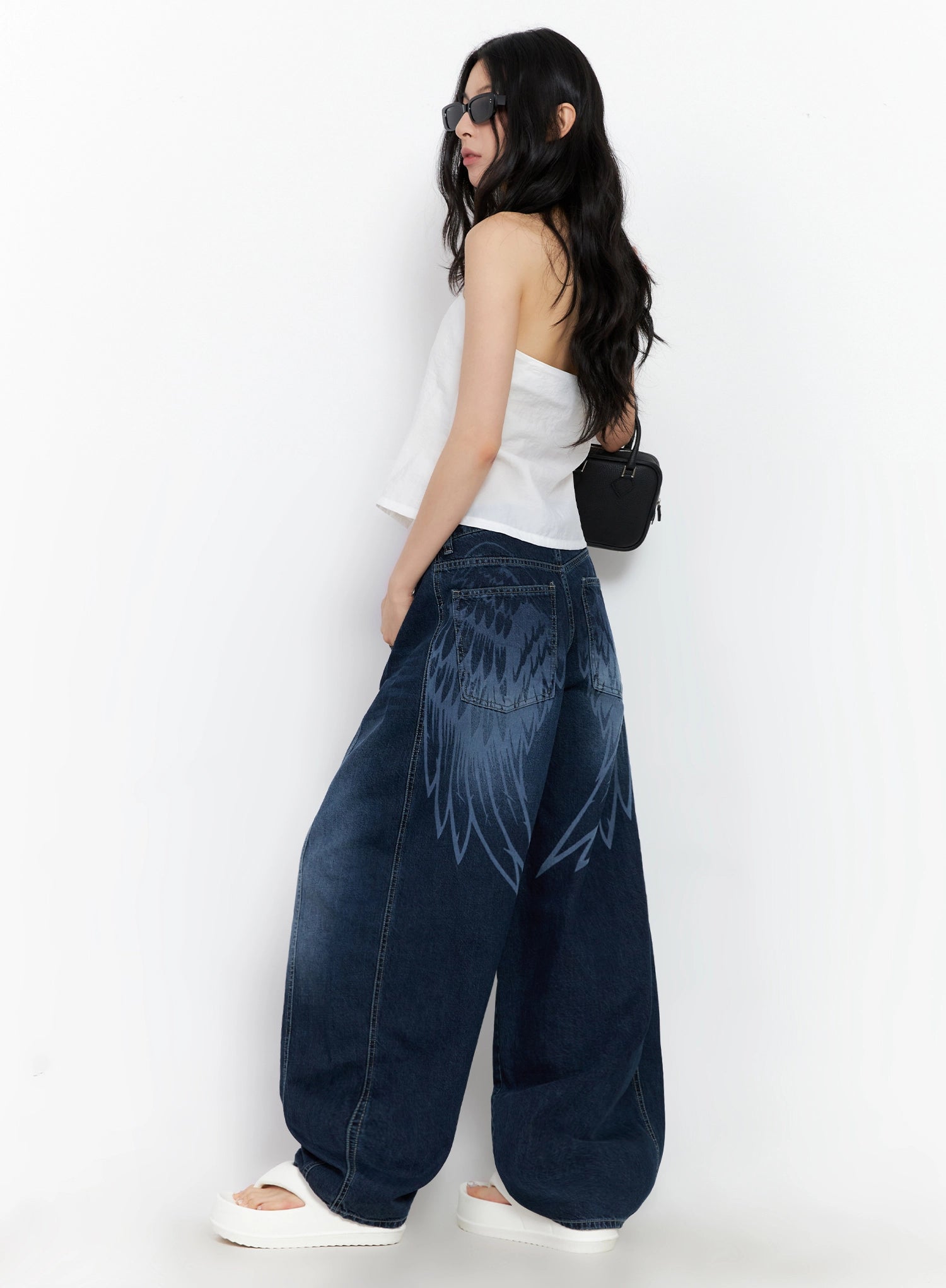 LEWKIN Sohee Angel Wing Print Wide-Leg Jeans IG508 in dark blue, back-angle view on model, washed cotton wide-fit silhouette with bold angel wing print, styled with white tube top and mini bag.
