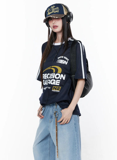 Oversized Sporty Graphic Tee CU519 in dark blue, angled front on model with cap and headphones, mesh fabric with white side stripes, racing graphic, styled with wide-leg jeans and backpack.