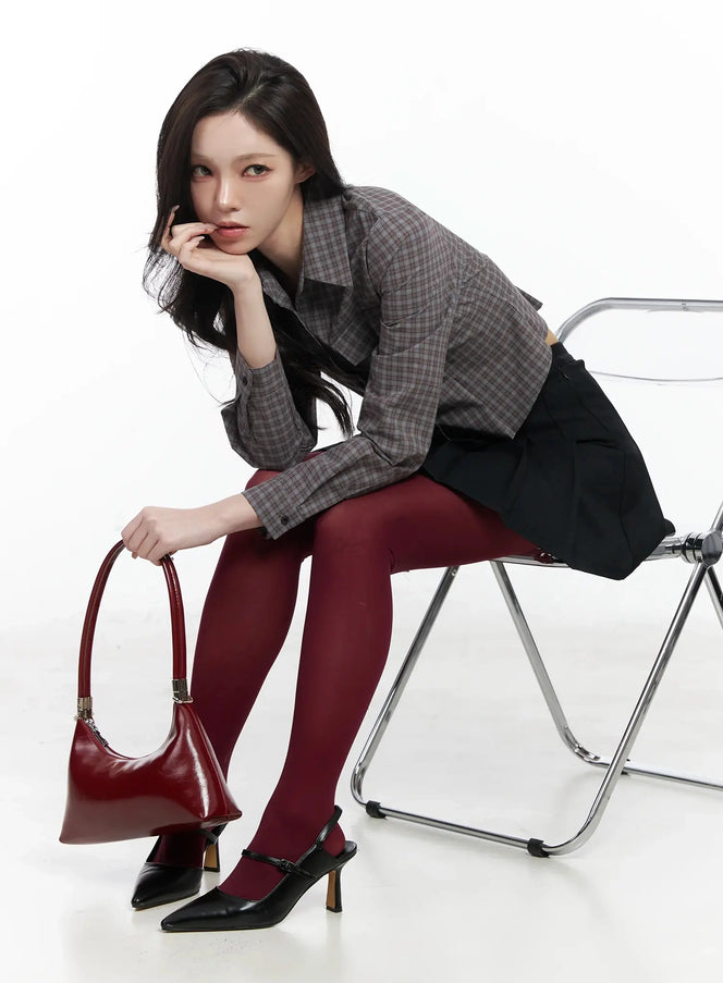 LEWKIN Checkered Crop Shirt IJ528 in dark brown, 3/4 editorial shot of model seated on folding chair, slim-fit cotton check long sleeve, styled with black pleated mini skirt, burgundy tights, and red bag.