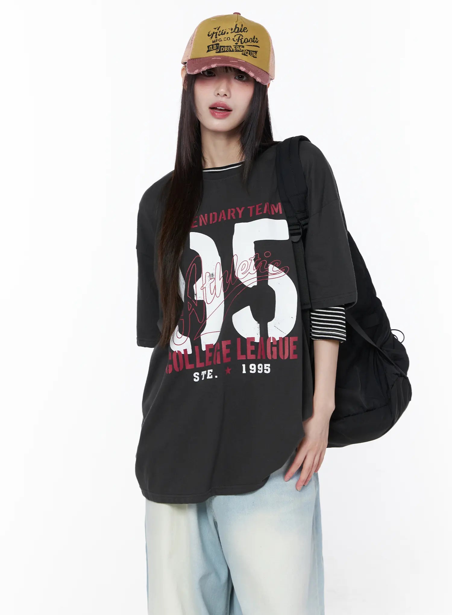 LEWKIN Oversized Graphic Tee CU519 in dark gray, front view on model wearing vintage cap and backpack, drop-shoulder short sleeve with collegiate 95 print, layered over striped top, styled with light blue wide-leg jeans.