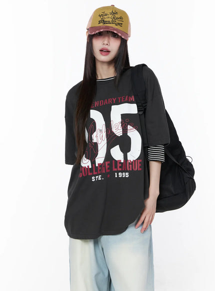 LEWKIN Oversized Graphic Tee CU519 in dark gray, front view on model wearing vintage cap and backpack, drop-shoulder short sleeve with collegiate 95 print, layered over striped top, styled with light blue wide-leg jeans.
