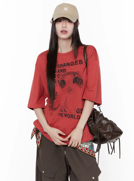 LEWKIN Oversized Cat Print Graphic Tee CU519 in dark red, front three-quarter shot on model wearing NY cap, drop-shoulder halftone cat print with slogan text, styled with brown cargo pants and leather bag.
