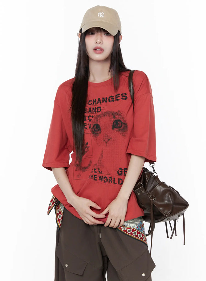 LEWKIN Oversized Cat Print Graphic Tee CU519 in dark red, front three-quarter shot on model wearing NY cap, drop-shoulder halftone cat print with slogan text, styled with brown cargo pants and leather bag.