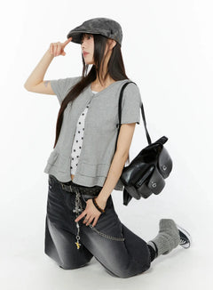 LEWKIN Frill Hem Loose Fit Button Cardigan IU518 in gray, three-quarter editorial shot on model kneeling, cotton short sleeve open cardigan with double frill hem, layered over star-print top, styled with dark jeans, cap, and black bag.