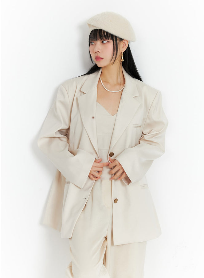 LEWKIN Oversized Blazer IF402 in light beige, front close-up on model buttoning the jacket, notched collar, long sleeves, styled with matching cami top and trousers, beret and pearl necklace.