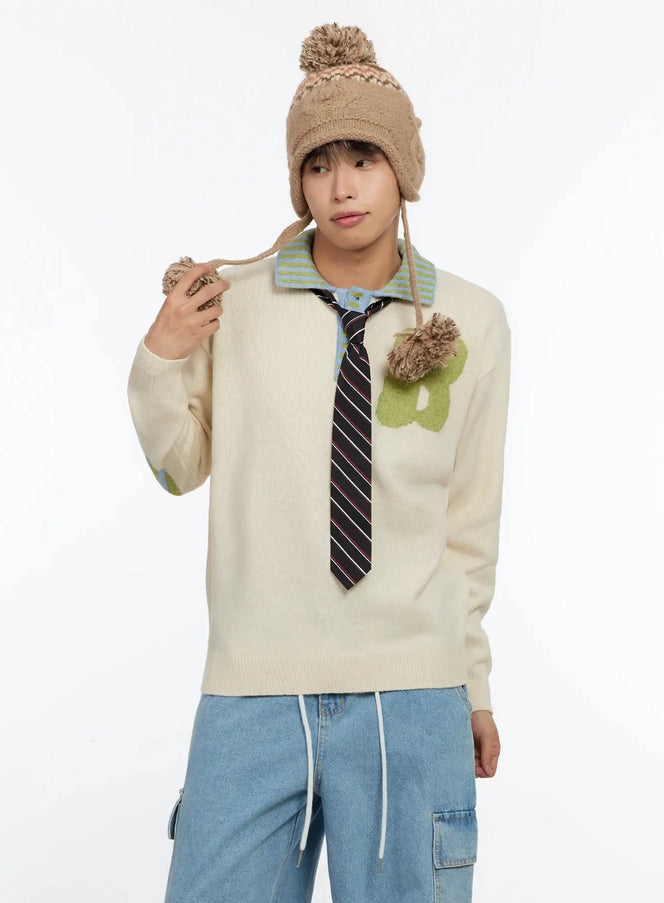 LEWKIN Men's Graphic Collar Sweater IN506 in light beige, half-body front on model with pom-pom hat, striped polo collar, green fuzzy B graphic, styled with striped tie and cargo jeans.