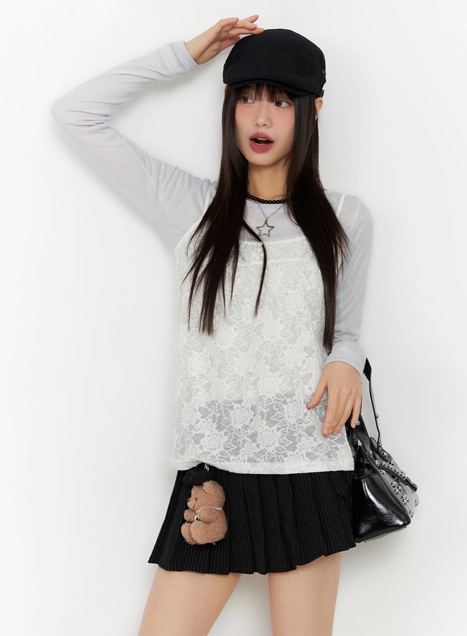 LEWKIN Floral Lace Camisole IN503 in light beige, full-length front on model, sheer floral lace over grey long-sleeve top, paired with black pleated mini skirt and baker boy cap.