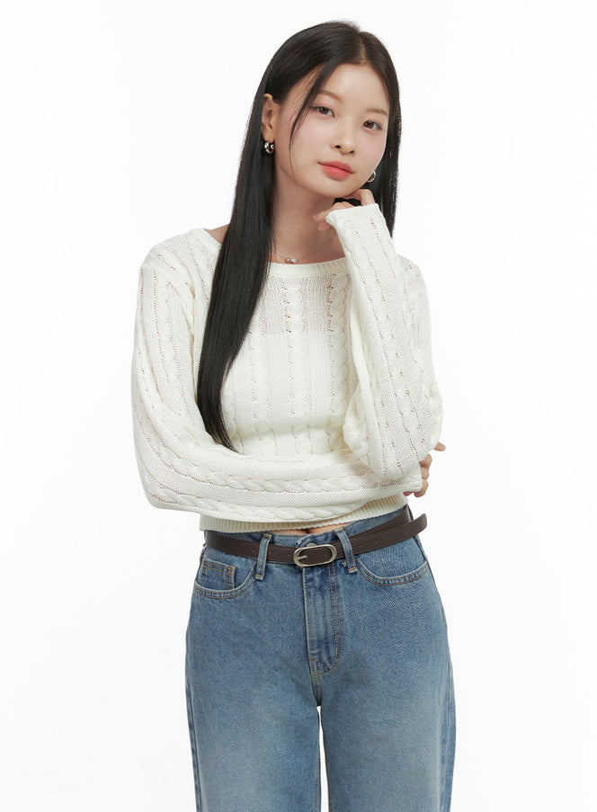 LEWKIN SoftTouch Wool Blend Top OS411 in light beige, front close-up on model with hand at chin, cable-knit crop sweater, round neck, long sleeves, paired with blue wide-leg jeans and brown belt.
