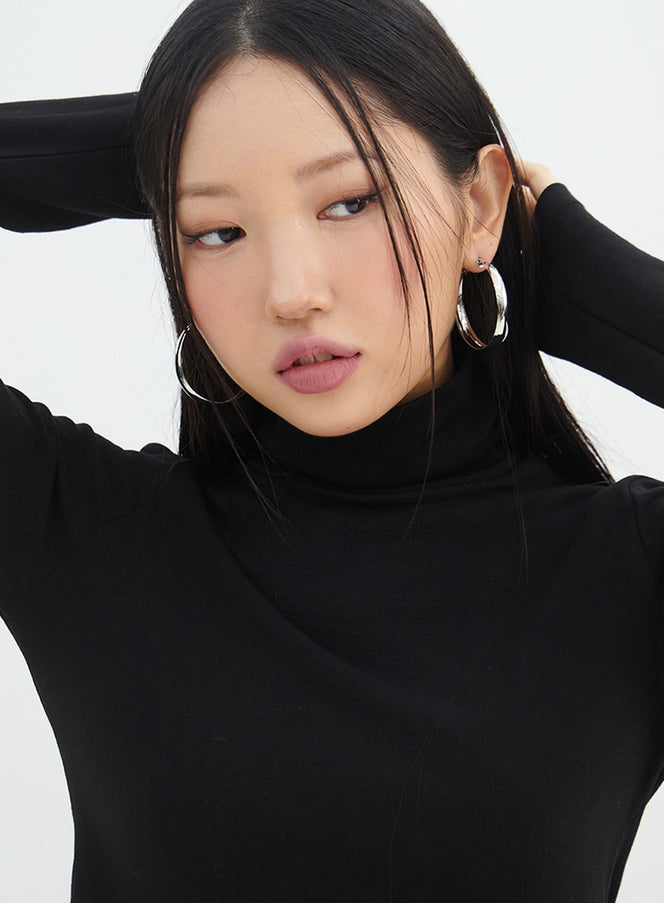 LEWKIN Chunky Hoop Earrings IN317 in light gray, worn on model, front close-up portrait, polished brass hoops paired with black turtleneck, hands raised behind head.