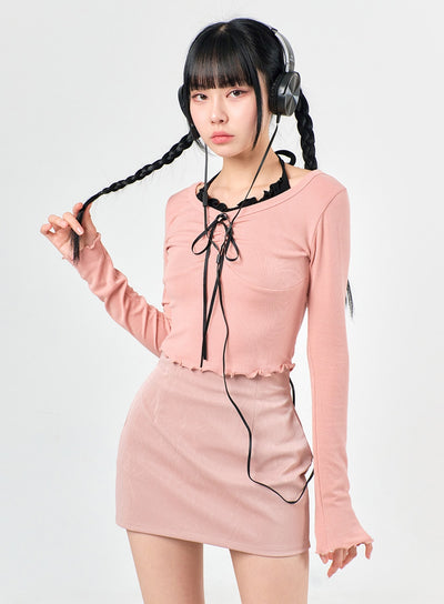 LEWKIN Ribbon Halter Shirring Crop Top IJ430 in Pink, front close-up on model, slim-fit ribbed long sleeve with black ribbon tie and ruffle hem, paired with pink mini skirt.