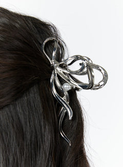 LEWKIN Bow Pearl Detail Claw Clip IY511 in Silver, extreme close-up worn in dark hair, open-work metallic bow silhouette with flowing tendrils and single pearl accent.