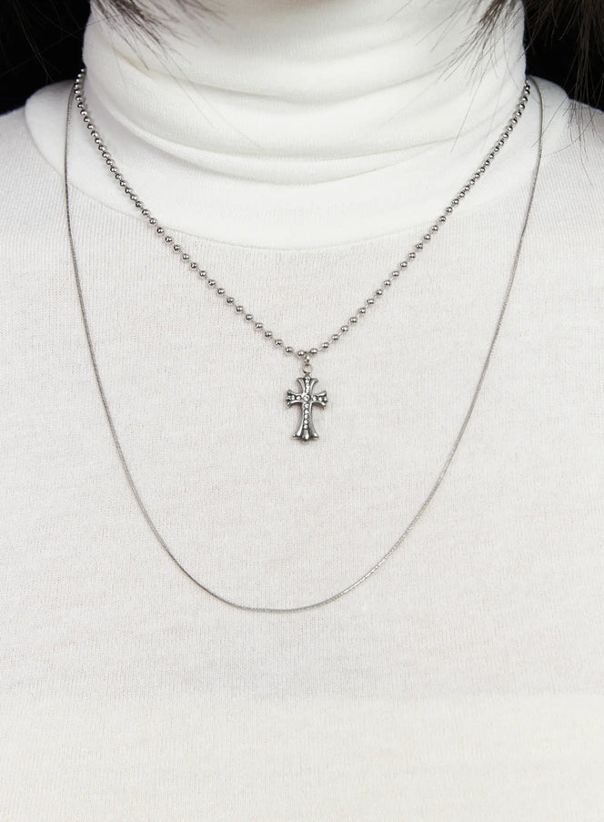 LEWKIN Layered Geometric Pendant Necklace CD530 in silver, chest close-up on model, ball chain with ornate cross pendant over snake chain, styled with white turtleneck.