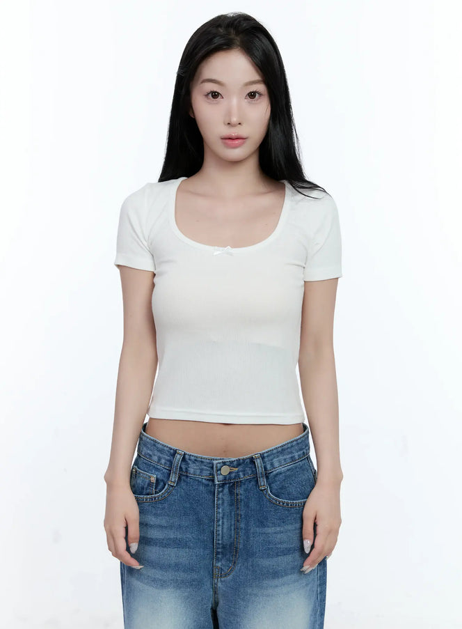 LEWKIN Ribbed U-Neck Crop Tee CL530 in white, front bust-up on model, slim-fit ribbed rayon crop with U-neckline, small satin bow detail, paired with blue wide-leg jeans.