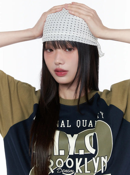 LEWKIN Polka Dot Head Scarf CU519 in White, front close-up on model pressing scarf to head with both hands, all-over black dot print, worn over bangs, paired with graphic raglan tee.