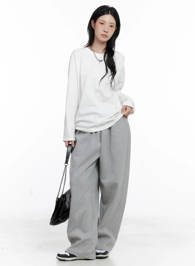 LEWKIN Basic Oversized Long Sleeve Tee CS529 in white, full-length front on model, drop shoulder cotton tee tucked into grey wide-leg sweatpants, styled with black chain bag and sneakers.