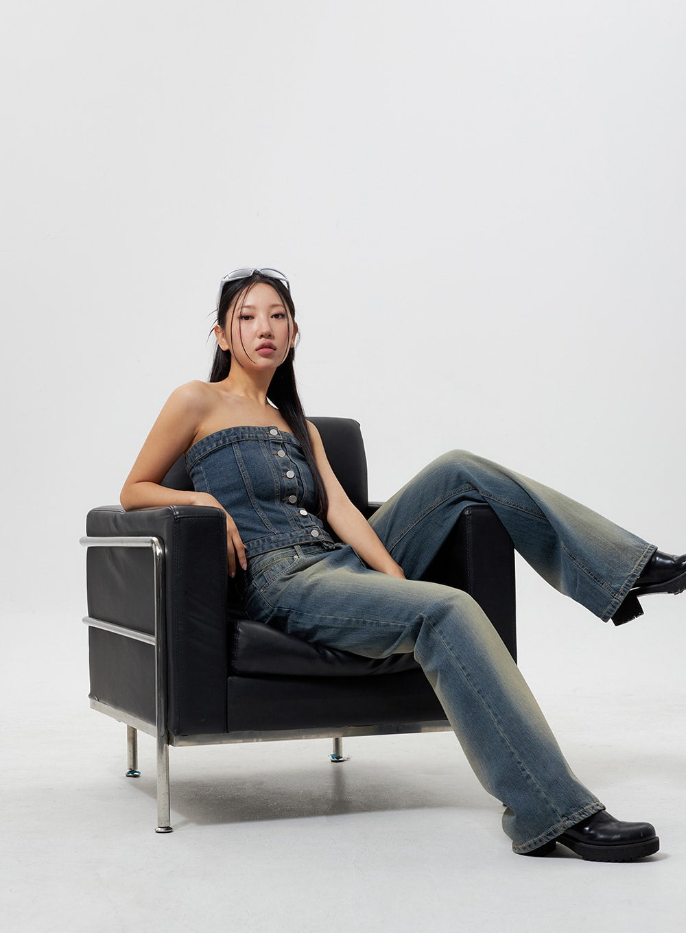 LEWKIN Low Rise Wide Leg Jeans CY323 in vintage blue, full-body seated shot on black leather chair, wide-leg silhouette with yellow-tinted fade wash, paired with denim tube top and black chunky boots.
