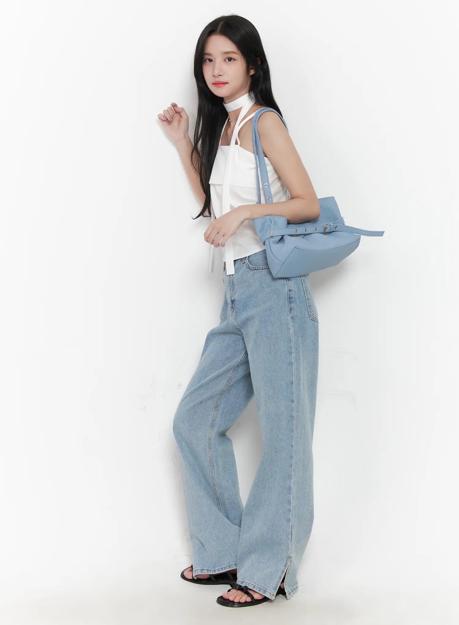 LEWKIN Hyuna Slit Straight-Fit Jeans CU525 in light blue, 3/4 side view on model leaning against wall, wide-fit washed denim with front slit hem, styled with white halter top and baby blue shoulder bag.