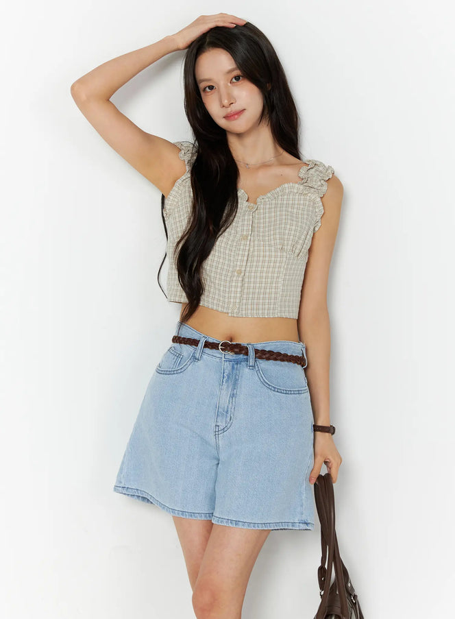LEWKIN Plaid Ruffle Sleeveless Top CU522 in beige, front 3/4 view on model, plaid crop top with ruffle straps and button front, styled with light blue denim shorts and braided belt.