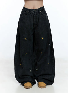 LEWKIN Wynter Star Embroidered Denim Jeans CG507 in black, front view on model cropped at waist, wide-leg cotton denim with scattered gold and silver star embroidery, worn with tan chunky shoes.