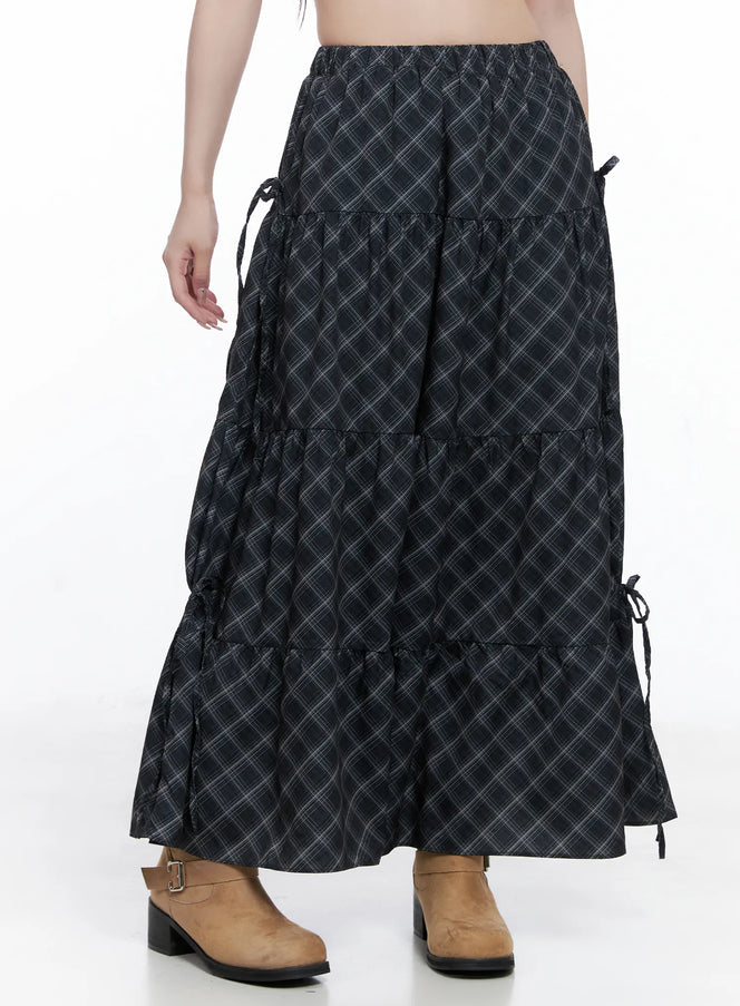 LEWKIN Plaid Maxi Skirt with Ribbon Details CG529 in black, side view on model, tiered ruffle hem with side ribbon ties, elastic waist, paired with tan ankle boots.