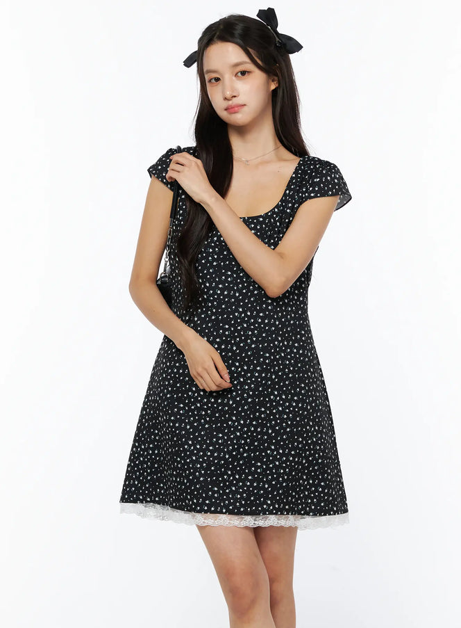 LEWKIN Floral Lace Trim Mini Dress CU522 in black, three-quarter front view on model, ditsy floral print with white lace hem trim, cap sleeves, square neckline, A-line silhouette.