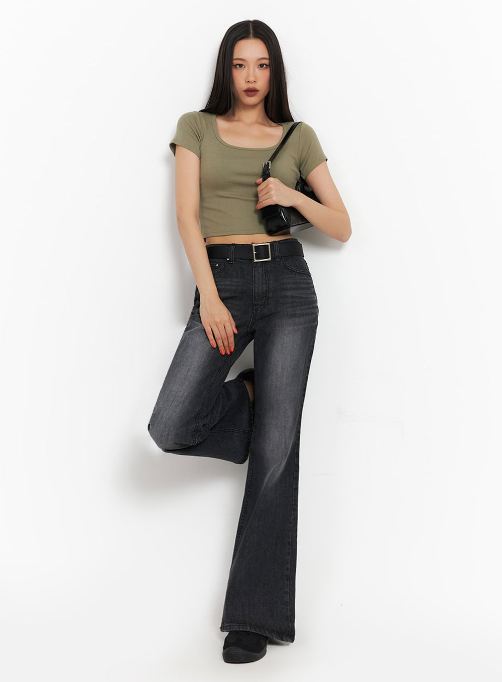 LEWKIN Joanna Washed Flared Jeans IA504 in washed black, full-body front on model with one leg raised, slim-fit bootcut flare, black belt, paired with olive crop top and black shoulder bag.